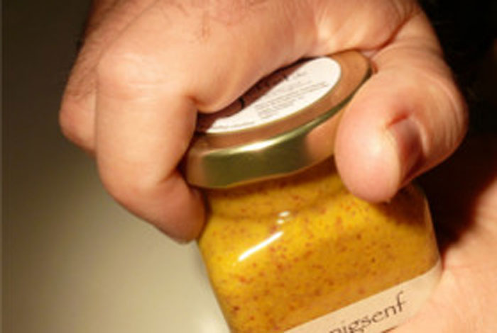 Ein Glas Honigsenf aus der Siegerländer Senfmanufaktur JEFFEL, das von einer Hand im Anschnitt geöffnet wird